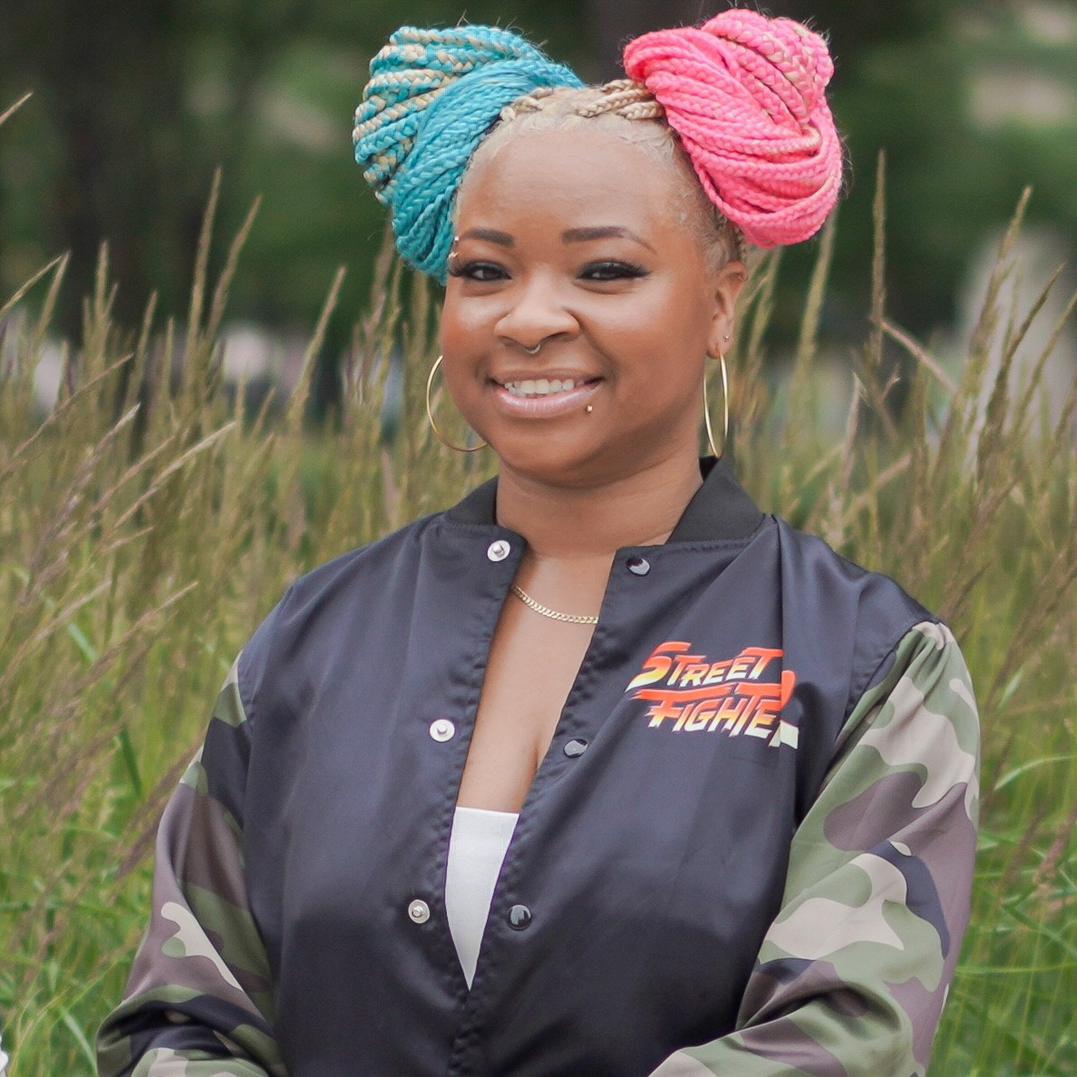 A headshot of Jeseekia in her favorite camo gaming-themed bomber jacket and signature pink and blue hair.